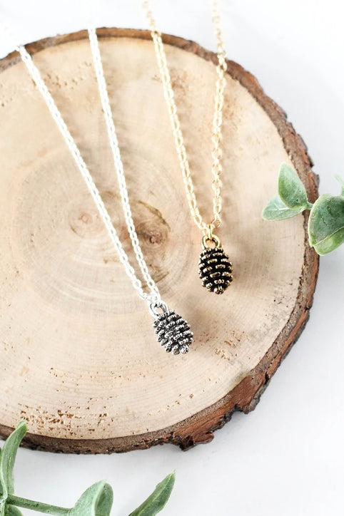 Tiny pine cone necklace by Birch Jewellery in silver and gold, styled on a stump of wood