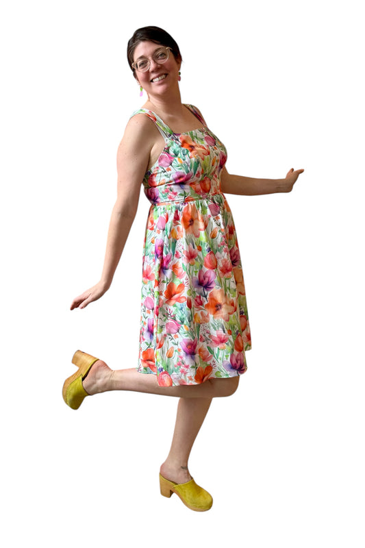 A woman wearing the Rue Floral Dress by Compli K, a midi-length tank dress with wide straps, a square neckline, a gathered waist and a full skirt. She is shown against a white background.