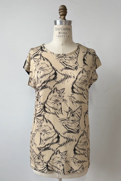 The Arto Tunic by Kollontai in Cats/Beige Print is shown on a mannequin against a grey background. It has a round neck, short extended sleeves, and a straight cut with a solid black back. 