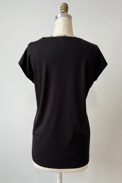 A back view of the Arto Tunic by Kollontain in Cats/Beige Print is shown on a mannequin against a grey background. It has a round neck, short extended sleeves, and a straight cut with a solid black back. 