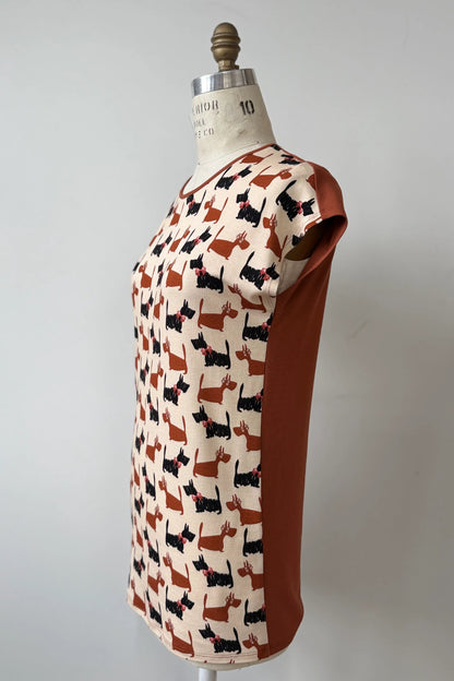 A side view of the Arto Tunic by Kollontain in Dogs/Rust Print is shown on a mannequin against a grey background. It has a round neck, short extended sleeves, and a straight cut with a solid rust coloured back. 