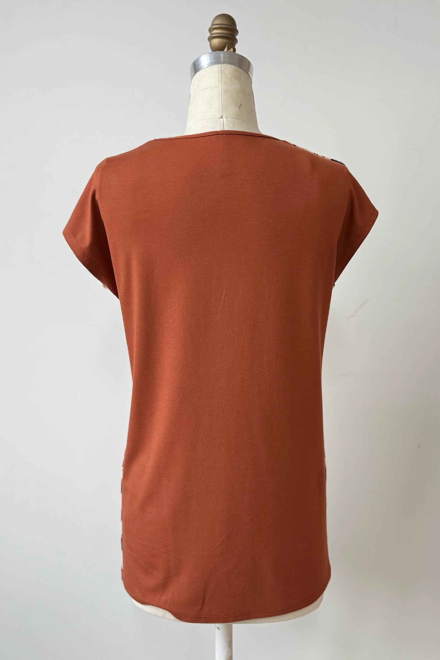 A back view of the Arto Tunic by Kollontain in Dogs/Rust Print is shown on a mannequin against a grey background. It has a round neck, short extended sleeves, and a straight cut with a solid rust coloured back. 