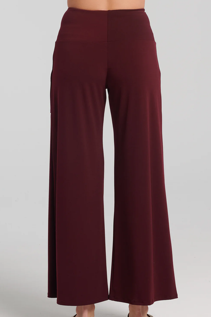 Waist-down back-view photo of woman wearing the Ramy Pants by Kollontai in Plum, standing in front of a white background 