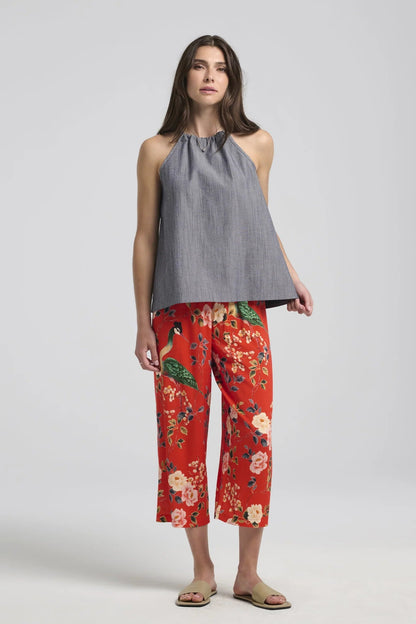 A woman wearing the Paraiso Pants by Kollontai in Red floral, with an elastic waist, wide cropped legs, and side slits at the hems. She's wearing them with the Semira Top in Denim and is standing in front of a white background. 