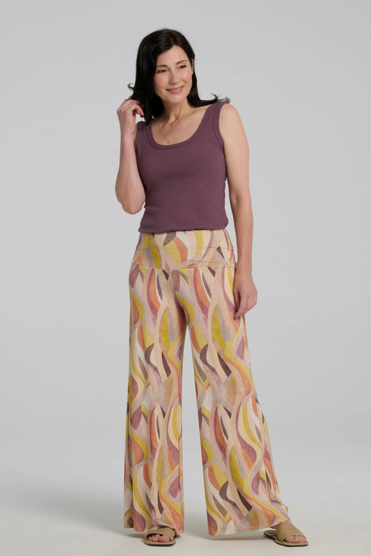 A woman wearing the Rina Camisole from Kollontai, a ribbed tank in stretchy bamboo with side straps and a scooped neck front and back.  She is wearing it with the Sorela Pants and standing in front of a white background. 