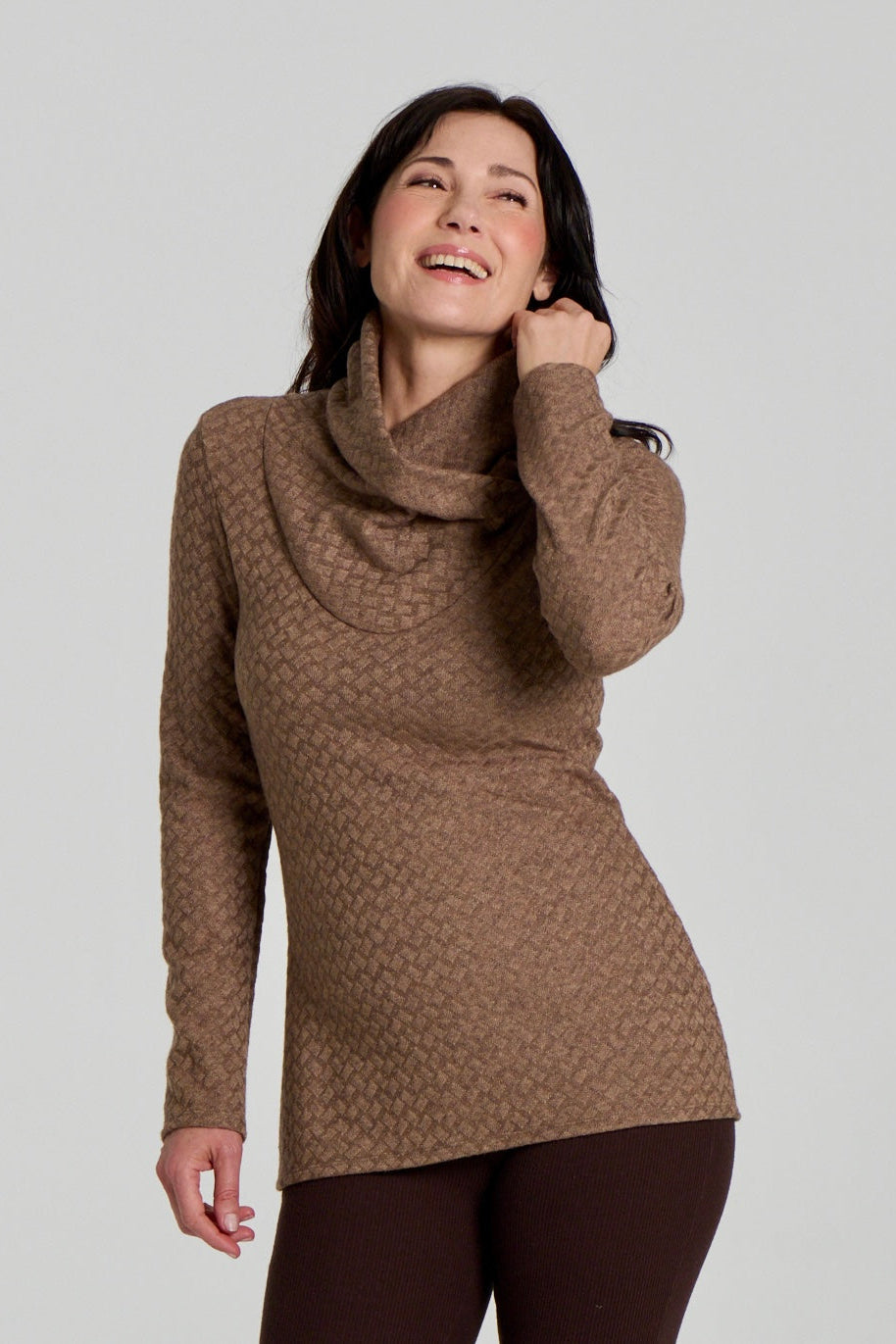 A woman wearing the Eloi Sweater by Kollontai in Brown, a slim fitting textured sweater with a large crossover collar. she is wearing it with brown pants and standing in front of a white background. 