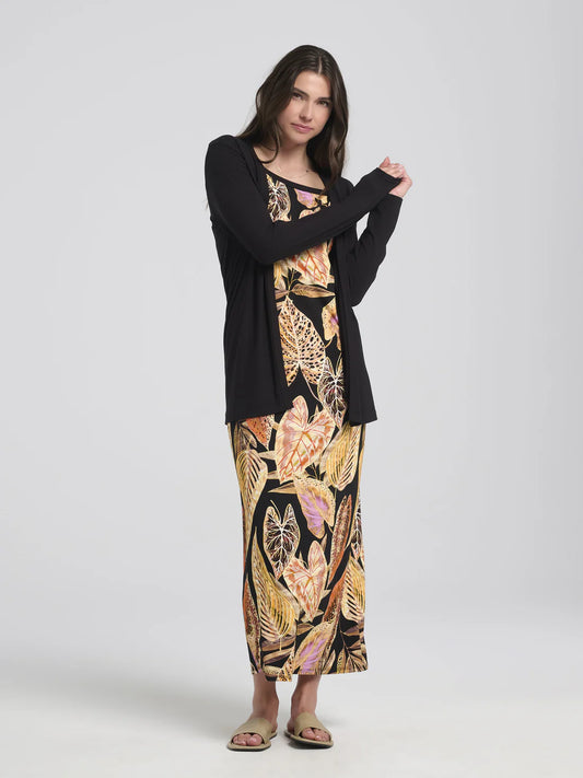 A woman wearing the Umay Cardigan by Kollontai in Black, an open hip-length cardigan made from light viscose. She is wearing it over a print dress and is standing in front of a white background. 