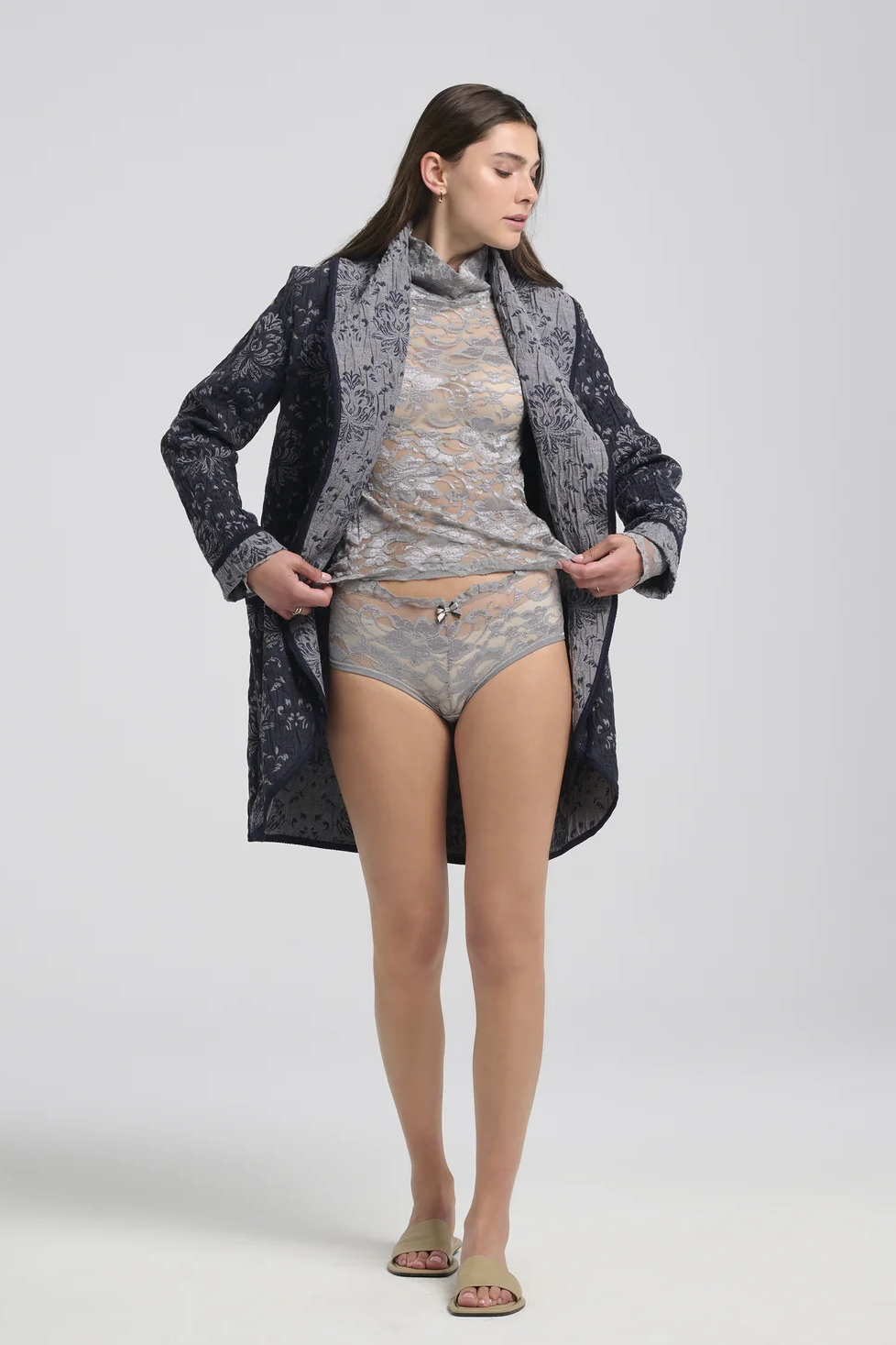 A woman wearing the Evelyn Jacket by Kollontai in a Blue jacquard fabric, with grey lingerie, standing in front of a white background