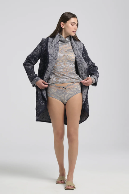 A woman wearing the Evelyn Jacket by Kollontai in a Blue jacquard fabric, with grey lingerie, standing in front of a white background