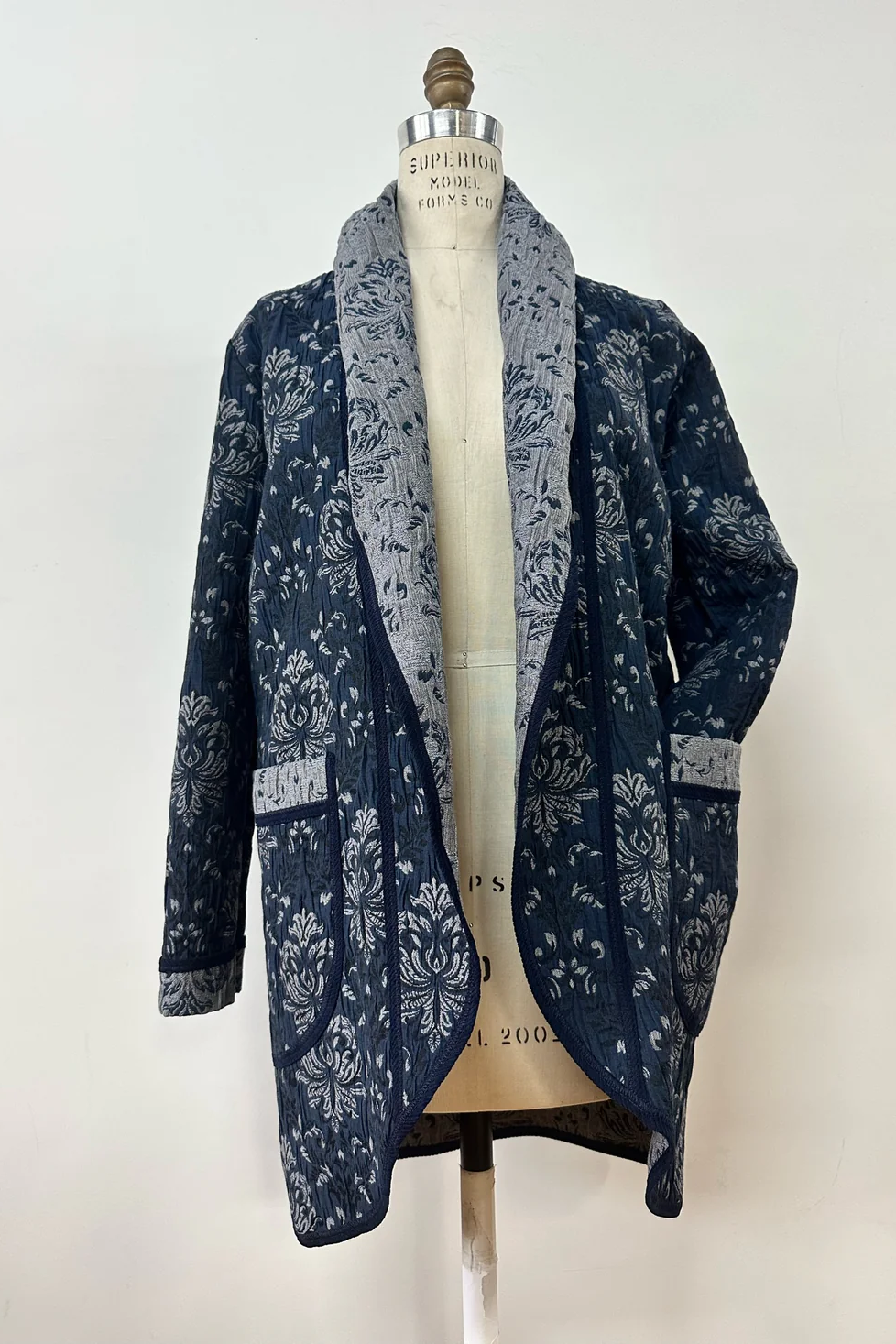 The Evelyn Jacket by Kollontai in a Blue jacquard fabric is shown on a mannequin in front of a white background