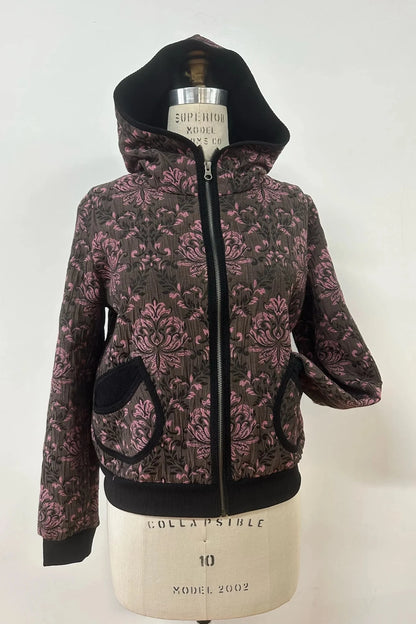 The Katniss Jacket by Kollontai in Pink, a bomber style jacket in jacquard fabric with a corduroy lined hood and rounded patch pockets, is shown on a mannequin