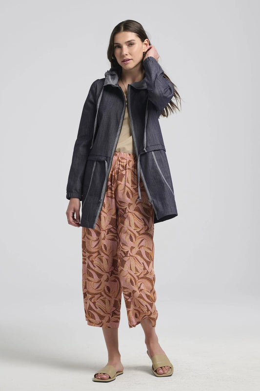 A woman wearing the Isiclora Pants by Kollontai in Cinnamon print, a lightweight pant with an elastic waist and flowing, cropped legs. She is wearing them with a denim jacket and standing in front of a white background. 