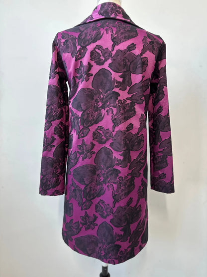 Back view of the Amarante Coat by Kollontai in Blackberry shown on a mannequin against a white background. It's a satin coat with an intricate floral pattern, a classic collar, button front, straight cut that hits above the knee, and large pockets. 