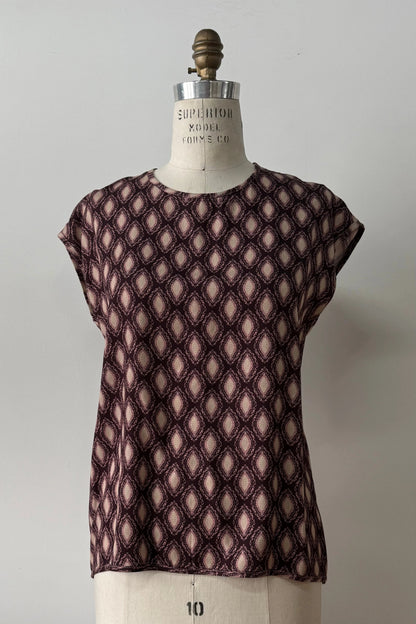 The Fanie Shirt by Kollontai, a relaxed fitting top with cape sleeves and a hi-low hem in a pink and plum geometric print, is shown on a mannequin against a white background. 