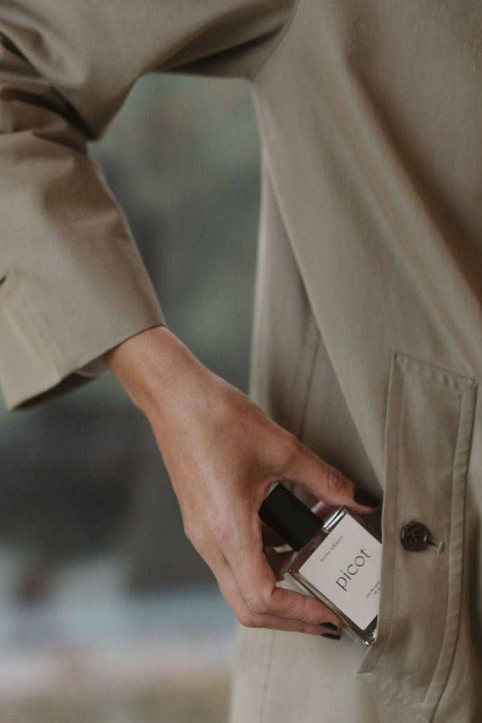 Person tucking holding a bottle of Picot Honey Tobacco eau de parfum into their coat pocket 