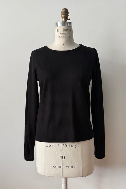 The Virginia Top by Kollontai in Black, a corduroy-textured top with inverted pleats on the long sleeves, a slim fit and a round neck, is shown on a mannequin against a grey background. 
