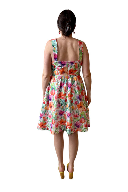 Back view of a woman wearing the Rue Floral Dress by Compli K, a midi-length tank dress with wide straps, a square neckline, a gathered waist and a full skirt. She is shown against a white background.