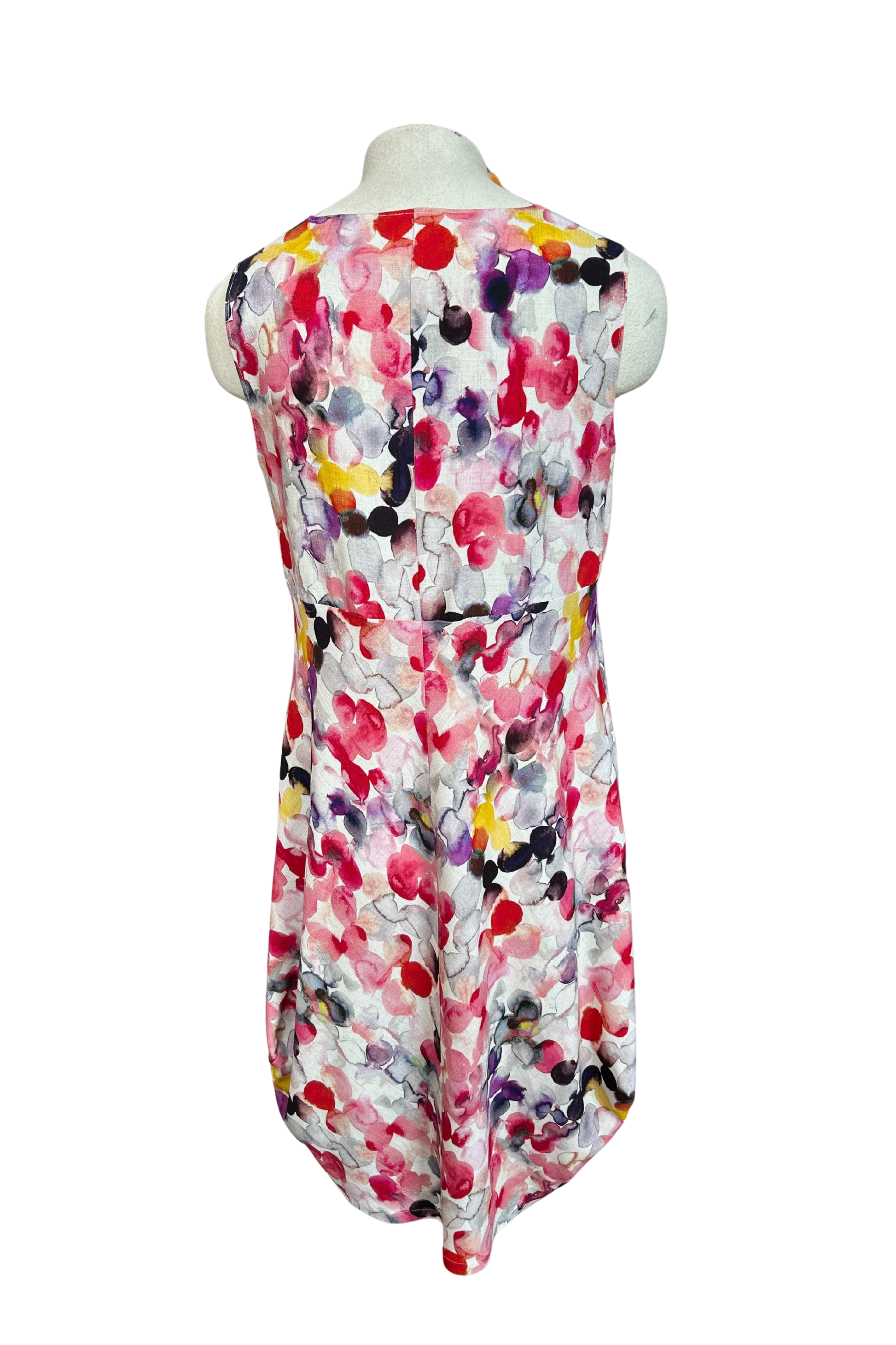 A back view of the Monica Dress by Solomia in Watercolour Print is shown on a mannequin against a white background. It's a sleeveless knee-length dress with a relaxed fit and uniquely angled bottom hem. 