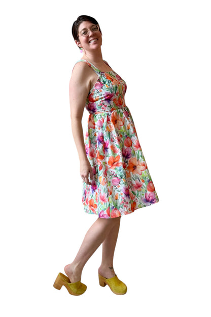 A woman wearing the Rue Floral Dress by Compli K, a midi-length tank dress with wide straps, a square neckline, a gathered waist and a full skirt. She is shown against a white background.