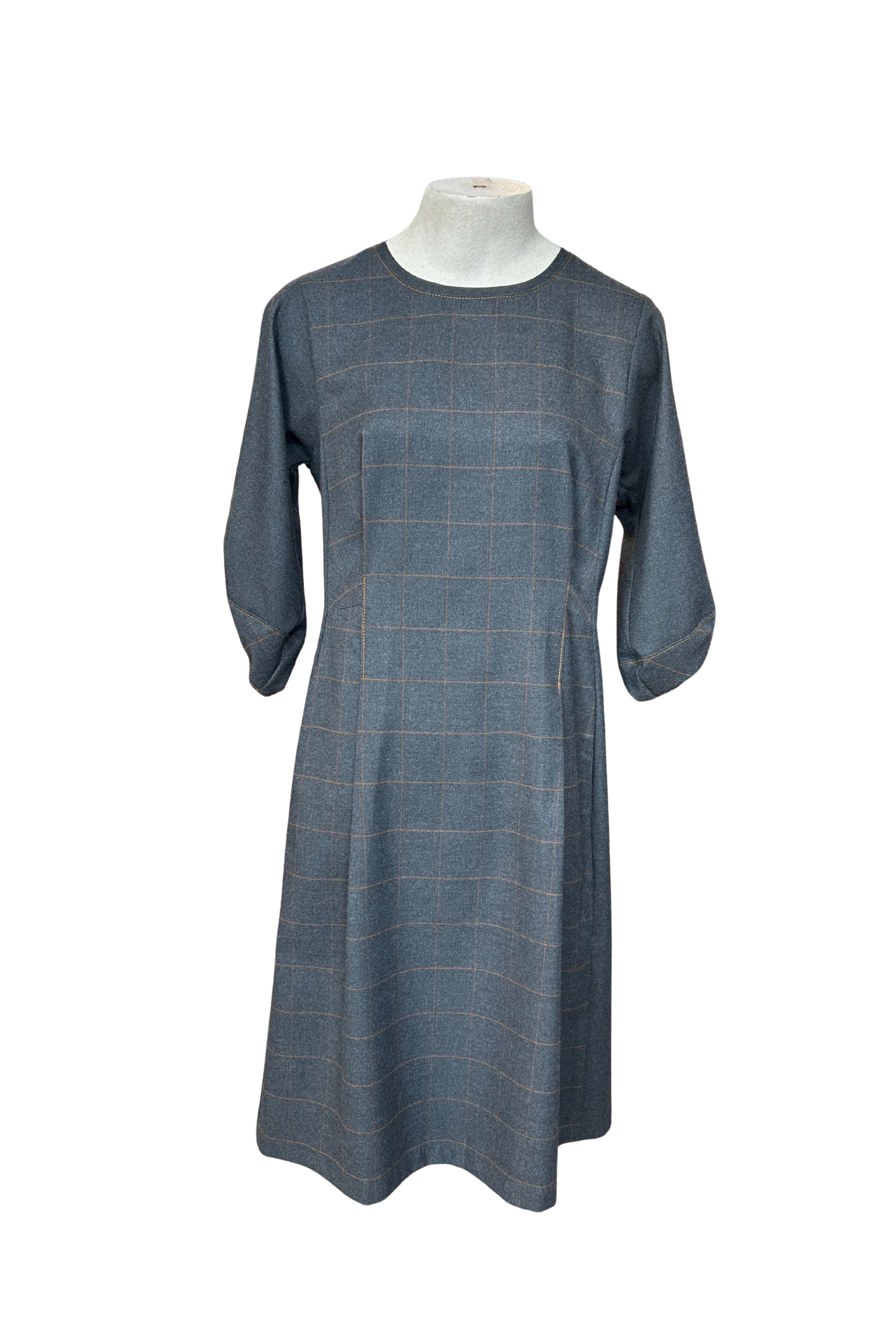 The Hanna Dress by Solomia in Grey is shown on a mannequin against a white background. This knee length dress has uniquely placed pleats and seams to create an architectural shape, with 3/4 length sleeves with structured cuffs. It has checked fabric on the front, back and cuffs, and solid grey fabric at the sides. 