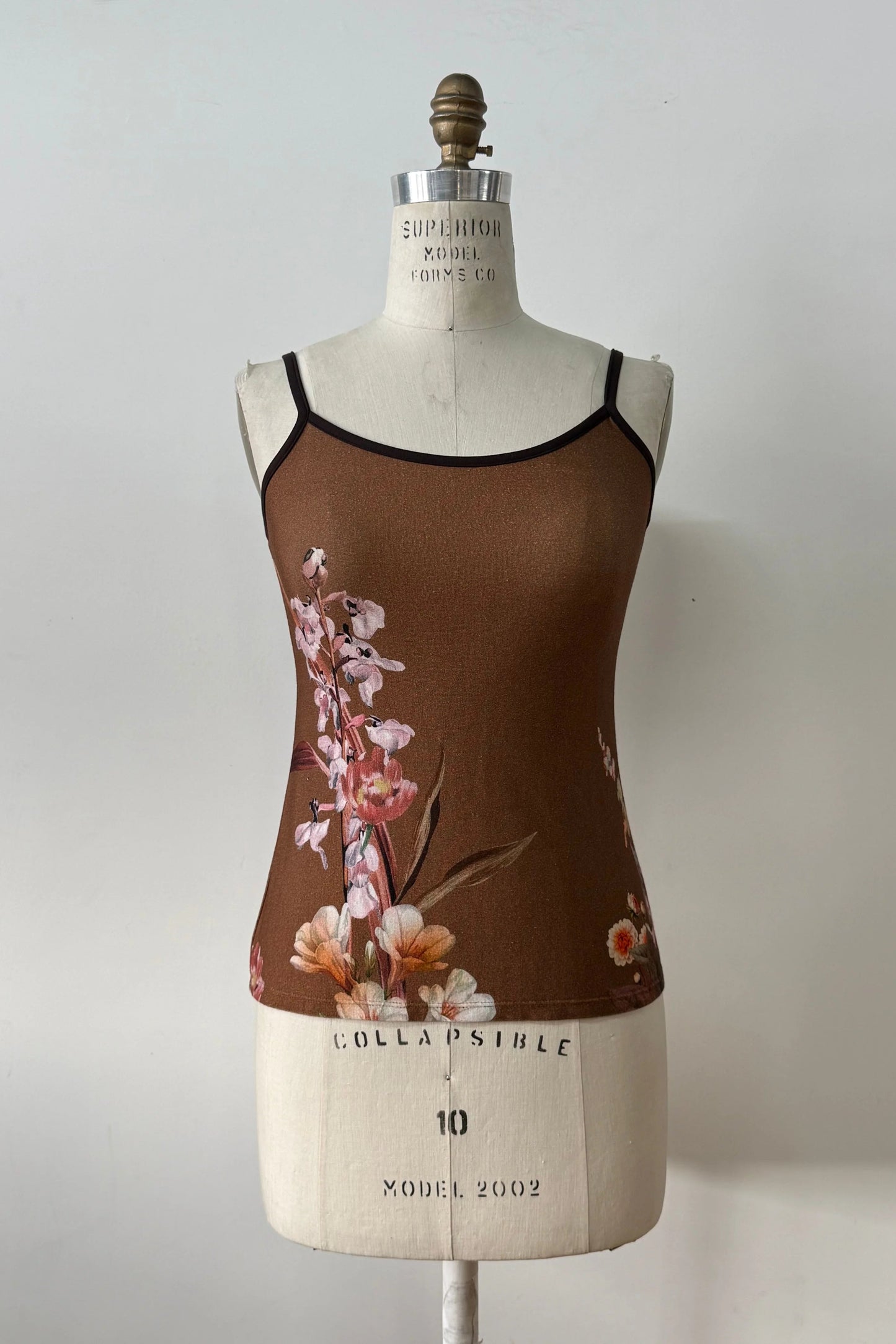 The Morganne Top by Kollontai, a brown floral tank top with spaghetti straps, is shown on a mannequin against a grey background