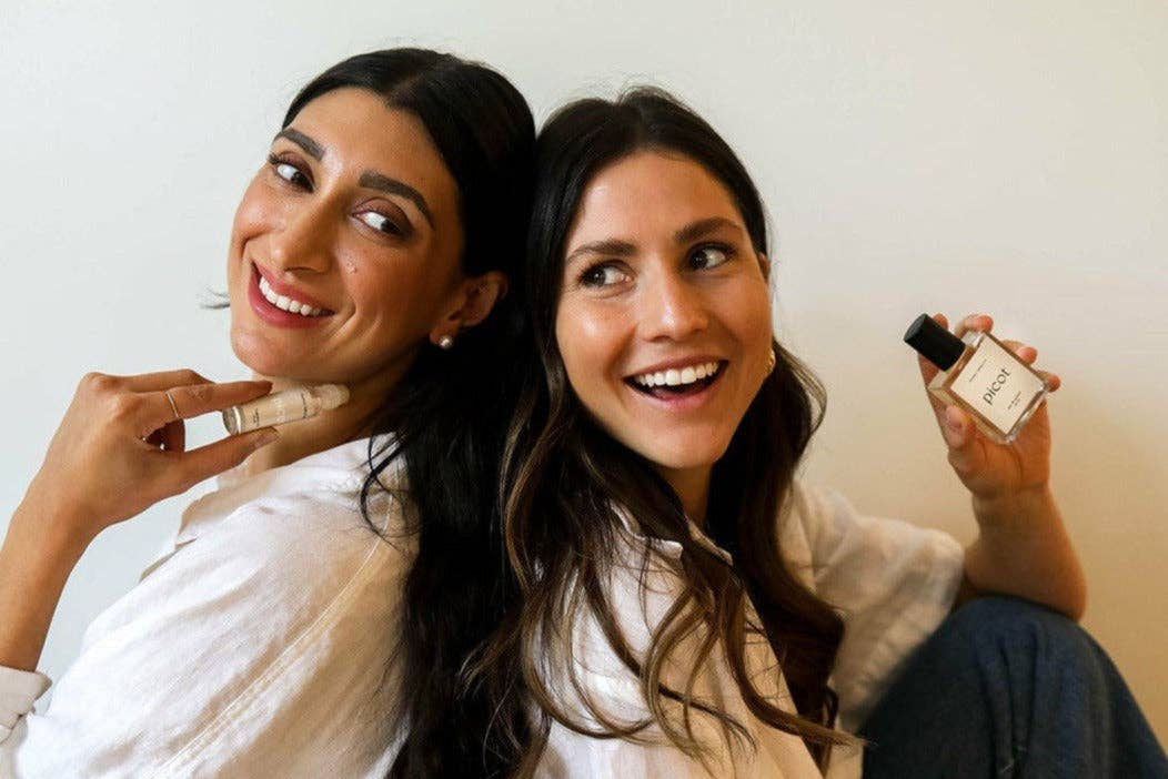 Two women holding Picot perfume products  against a plain background