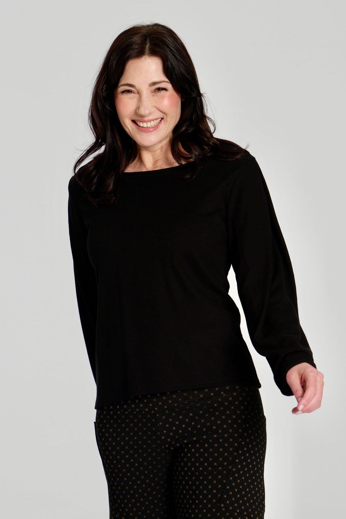 A woman wearing the Virginia Top by Kollontai in Black, a corduroy-textured top with inverted pleats on the long sleeves, a slim fit and a round neck. She is wearing it with the Susan pants in Black