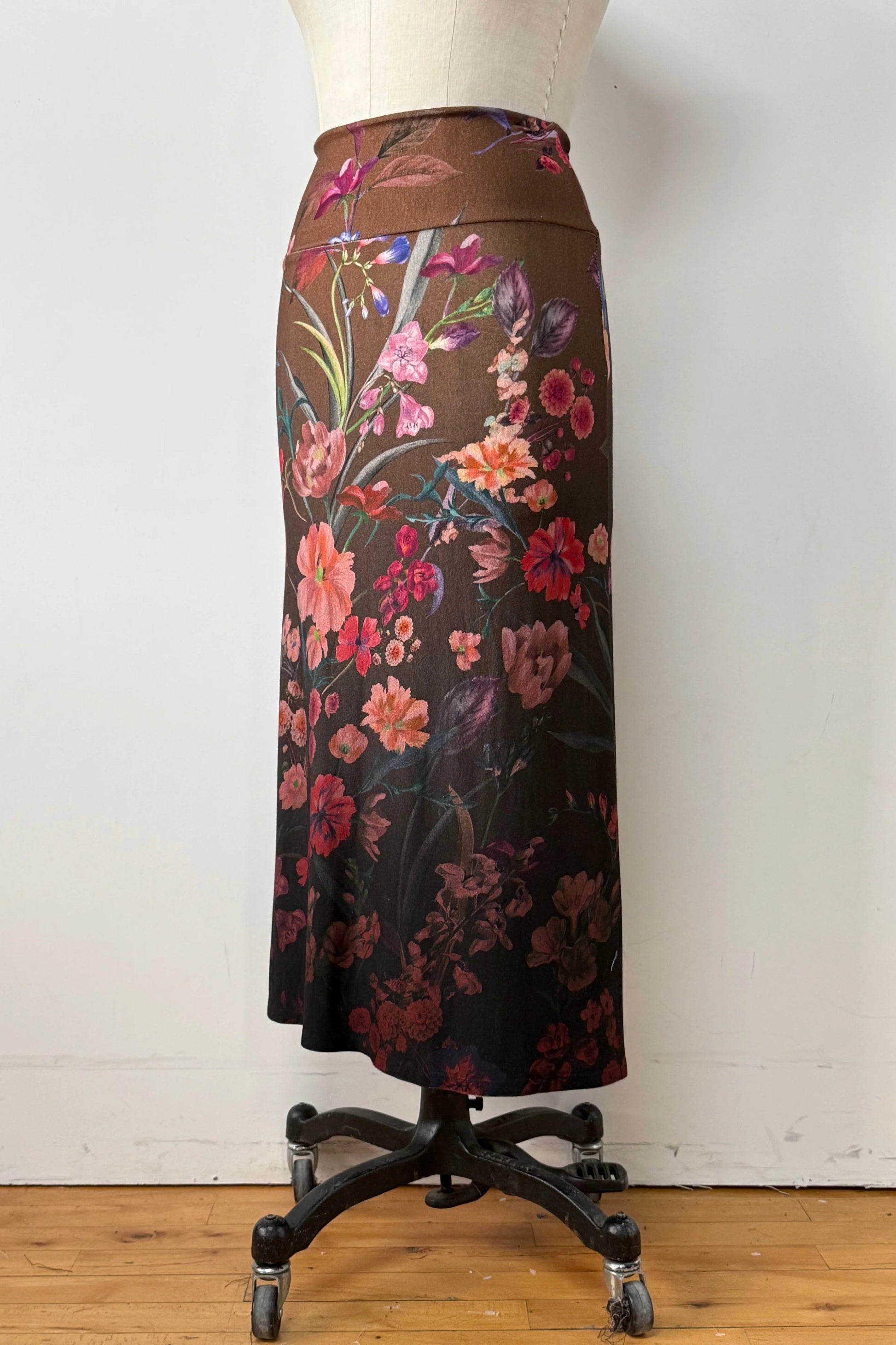 The Charlotte SKirt by Kollontai, a long slim cut brown skirt adorned with a floral pattern, is shown on a mannequin against a white background. 