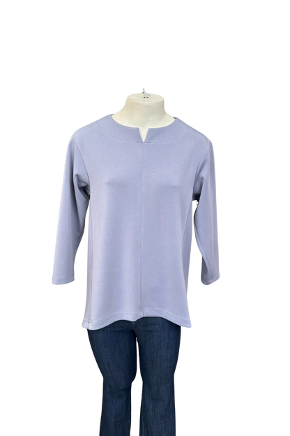 The Vanessa Top by Solomia in Blue is shown on a mannequin against a white background. It has a notched neckline, 3/4 sleeves, a rounded hi-low hemline, and a vertical seam down the front. 