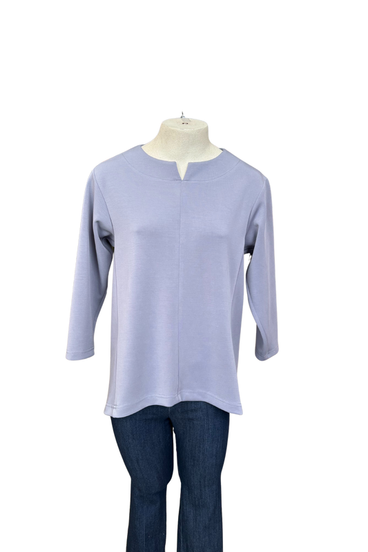 The Vanessa Top by Solomia in Blue is shown on a mannequin against a white background. It has a notched neckline, 3/4 sleeves, a rounded hi-low hemline, and a vertical seam down the front. 