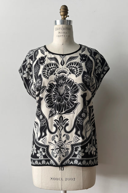 The Malo T-shirt from Kollontai, featuring a floral and panther print in black-on-ivory on the front, cap sleeves, and a solid black back, is shown on a mannequin in front of a grey background 