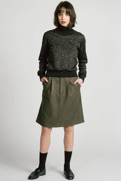 A woman wearing the Crux Sweatshirt by Allison Wonderland in Animal Print. she is wearing it with a grey skirt and standing in front of a white background. 