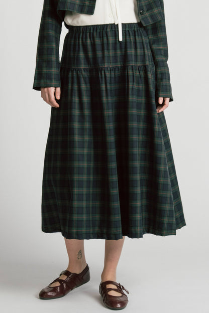 Waist down view of a woman wearing the Pegasus Skirt in Plaid by Allison Wonderland, a midi length A-line skirt with an elastic waist, with the matching Libra bolero and a white top. She is standing in front of a white background