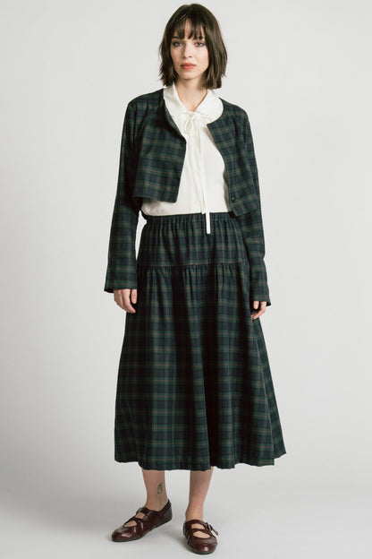 A woman wearing the Pegasus Skirt in Plaid by Allison Wonderland, a midi length A-line skirt with an elastic waist, with the matching Libra bolero and a white top. She is standing in front of a white background. 