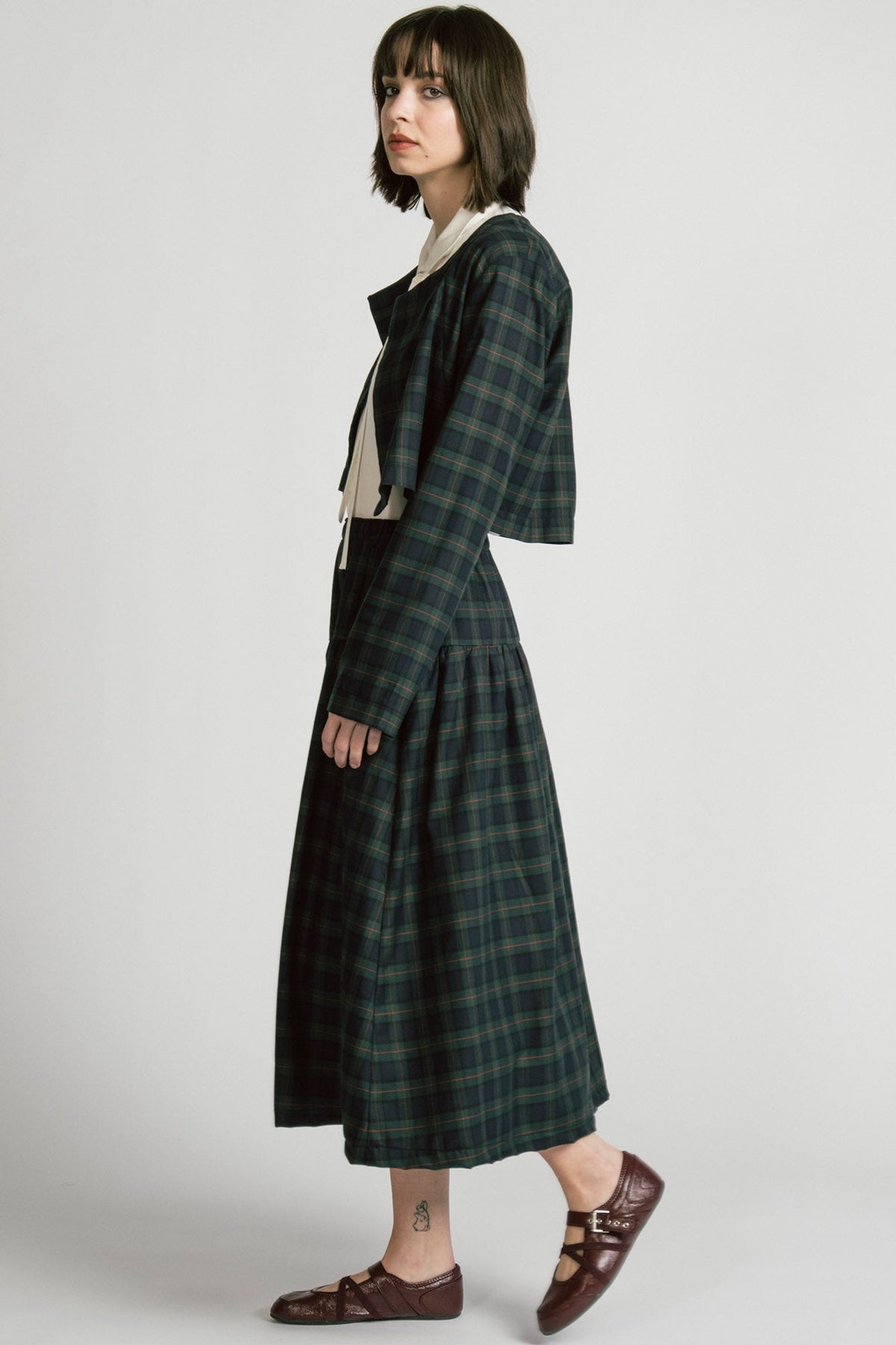 Side view of a woman wearing the Pegasus Skirt in Plaid by Allison Wonderland, a midi length A-line skirt with an elastic waist, with the matching Libra bolero and a white top. She is standing in front of a white background