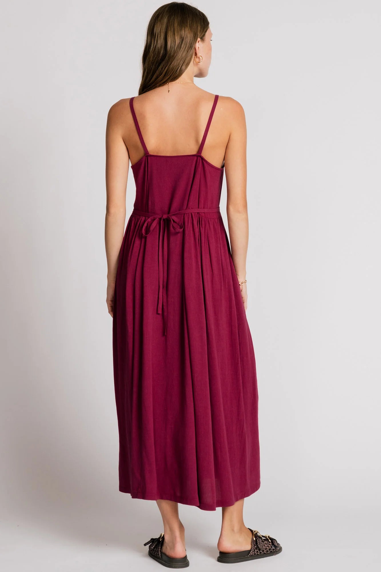 Back view of a woman wearing the Swan Dress by Allison Wonderland in Pink, a maxi dress with spaghetti straps, and ties at the waist. 