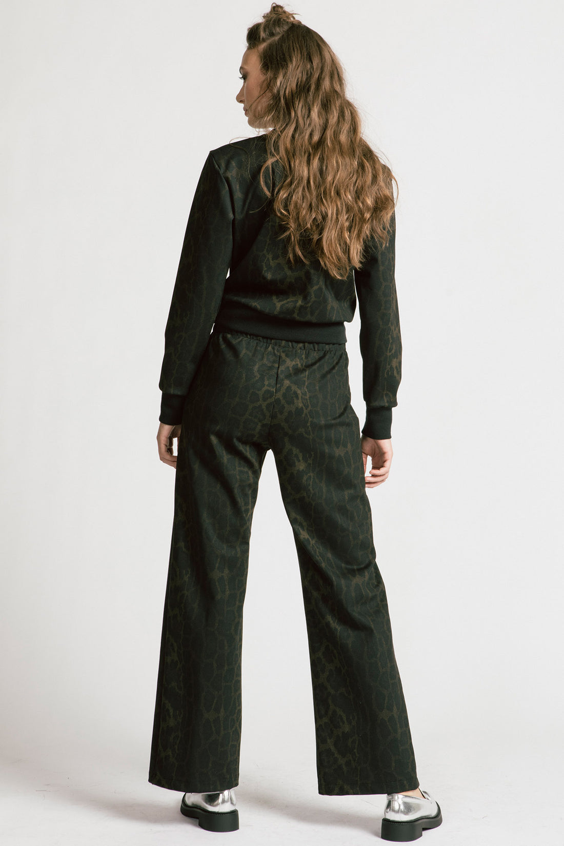 Back view of a woman wearing the Gone Top by Allison Wonderland in Leopard, a classic crewneck, with matching pants. She is standing in front of a white background. 