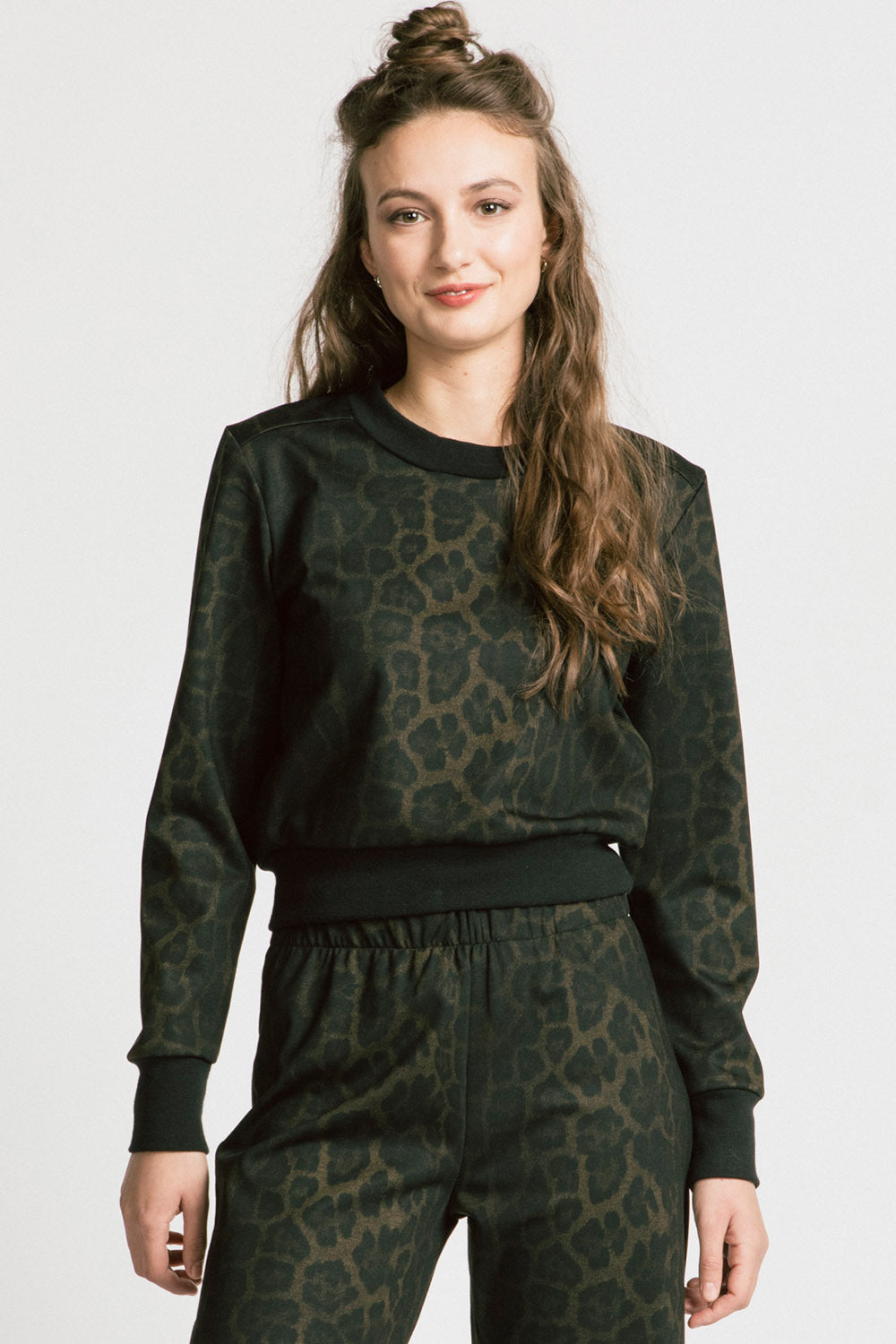 A woman wearing A woman wearing the Gone Top by Allison Wonderland in Leopard, a classic crewneck, with matching pants. She is standing in front of a white background. 