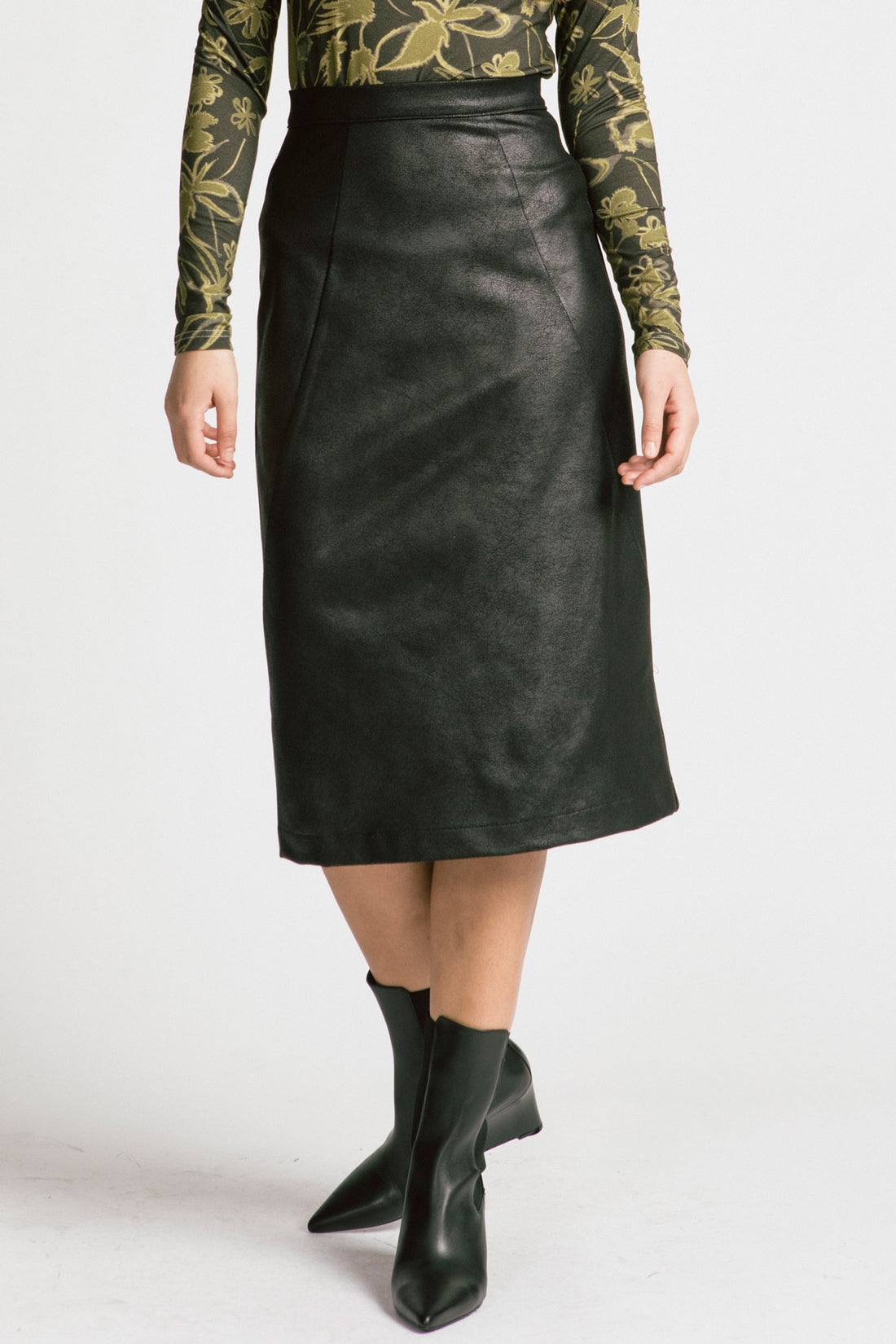 Waist down view of a woman wearing the Graduate Skirt by Allison Wonderland in black Leatherette, a slim midi-length pencil skirt in faux leather with a two-way zipper at the back. She is wearing it with the Rebecca Turtleneck and standing in front of a white background. 