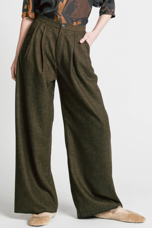 Waist-down view of a woman wearing the Memory Pant by Allison Wonderland in brown Herringbone print, wide-legged pants with front pleats, a zip and button closure, front pockets and back patch pockets. She is wearing them with the Flash Blouse in Horses print and standing in front of a white background. 