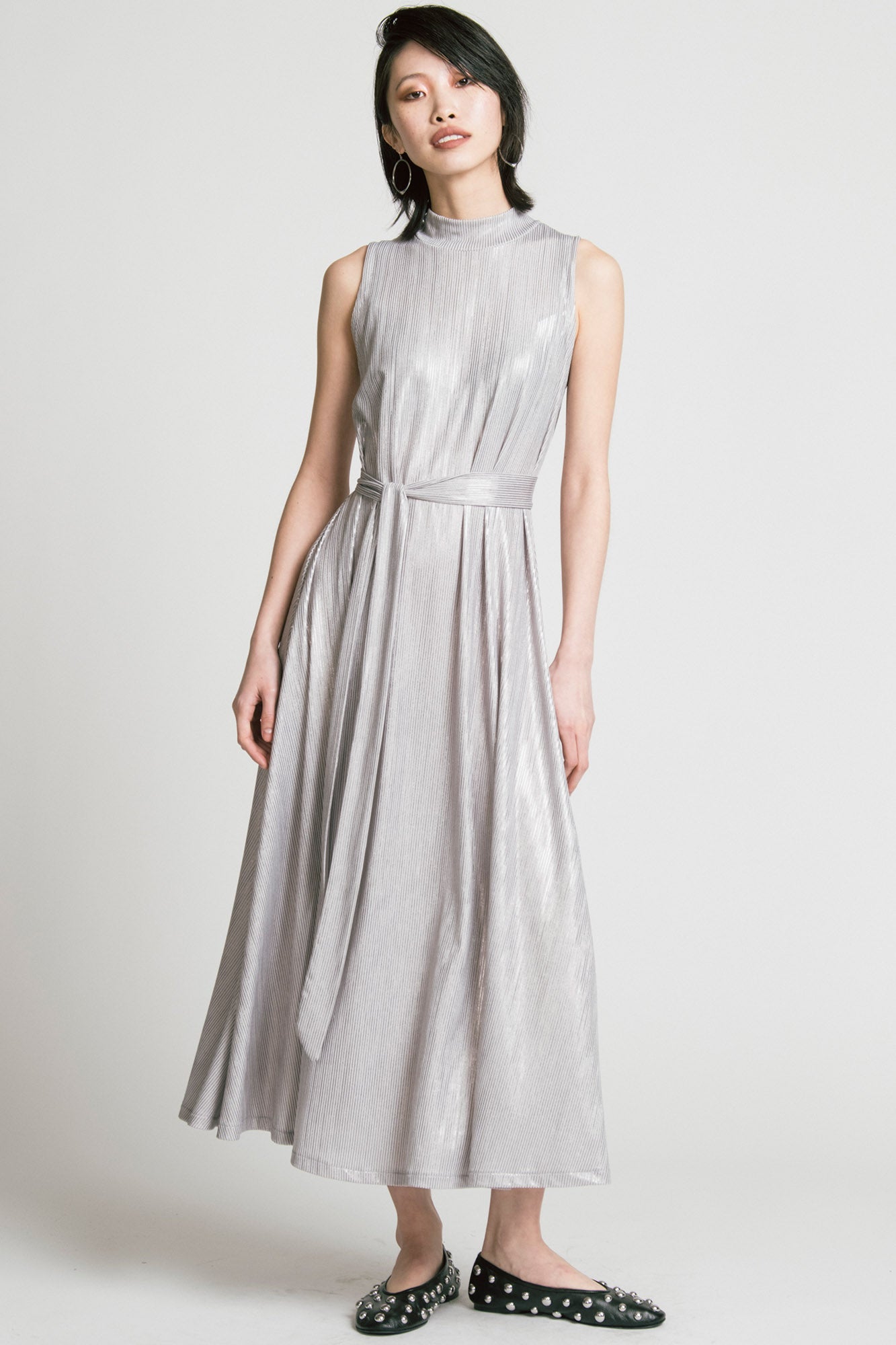 A woman wearing the Swing Dress by Allison Wonderland in Silver, a sleeveless mock neck maxi dress in shimmery fabric. 