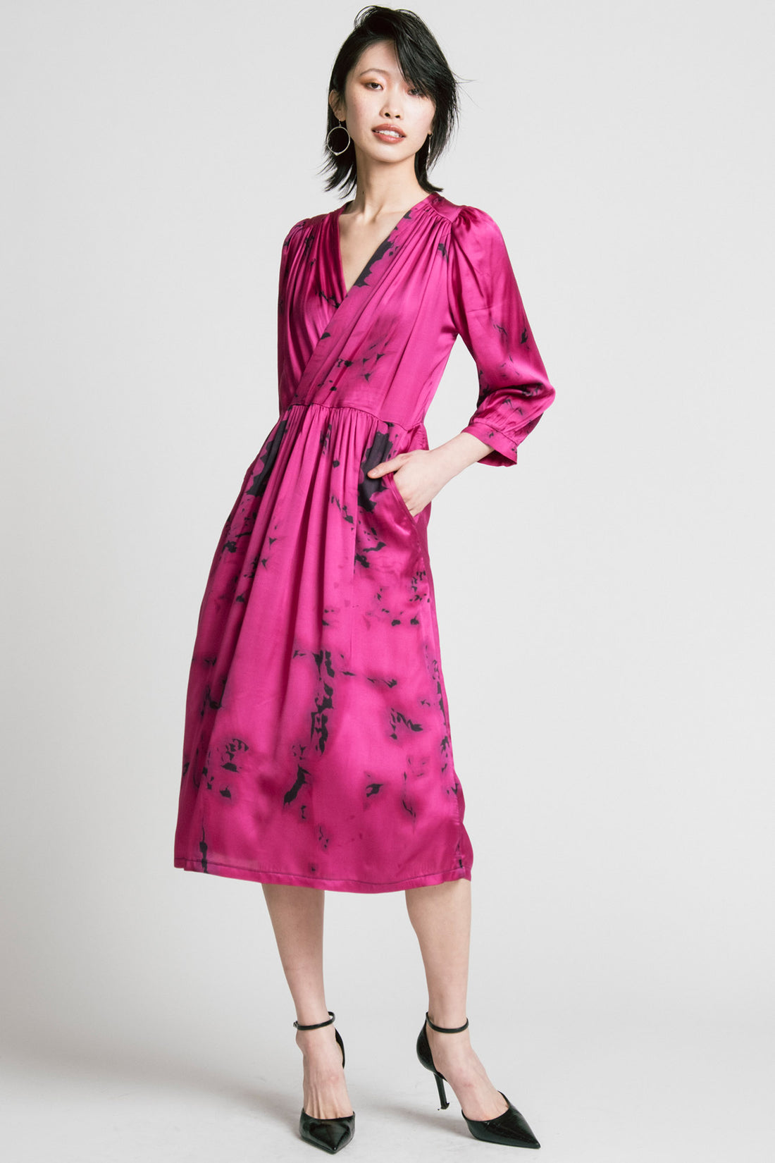 A woman wearing the Therapy Dress by Allison Wonderland in Pink Print, with a faux wrap front, gathers at the shoulders cuffs and waist, and a full midi-length skirt. She is standing in front of a white background. 
