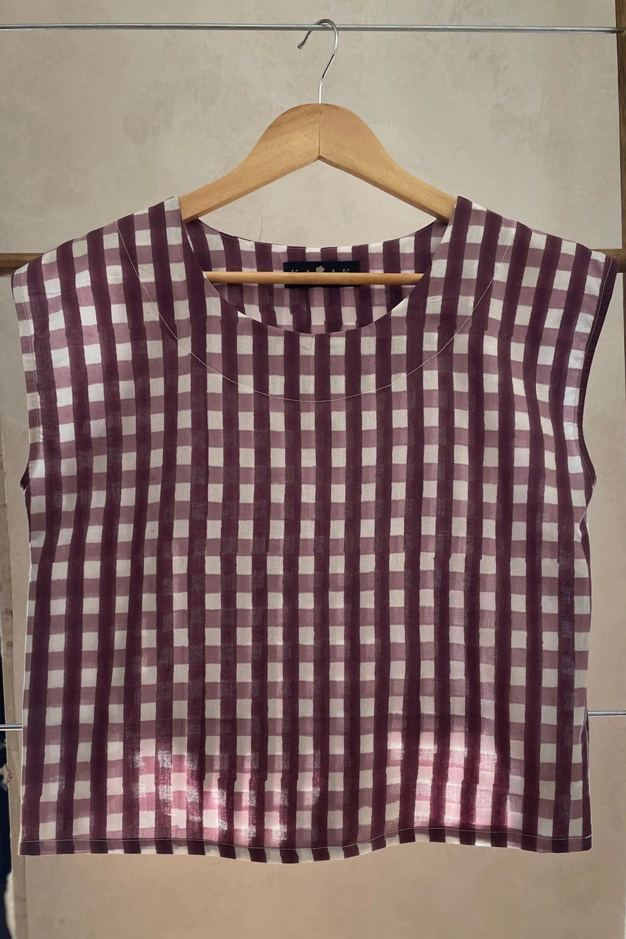 The Sandrigo Top from Kazak in Burgundy Gingham print, a cotton top with short extended sleeves and a wide round neck, is shown on a wooden hanger against a grey background. 