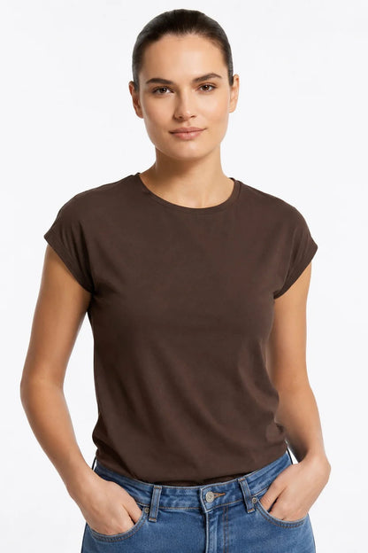 A woman wearing the Eowyn T-Shirt by Kollontai in Chocolate with jeans standing against a grey background. 