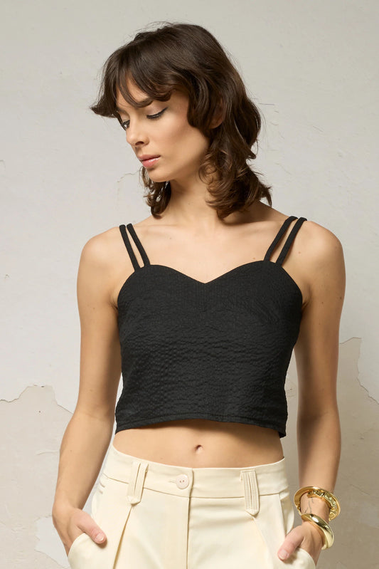 Waist up view of  woman wearing the Bia Cami by Cokluch in Black, a double strapped crop top with a sweetheart neckline. She is wearing it with beige pants against a neutral background