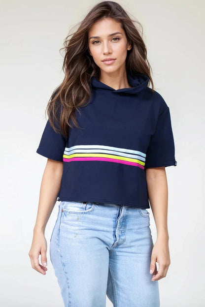3/4 shot of a woman wearing the Olive+Splash Bamboo T-Shirt Hoodie in Striped navy,  featuring short sleeves, a cropped fit, and a splash of bright stripes across the midsection with a vertical gold zipper detail at the right hemline. She is wearing it with jeans and standing in front of a white background. 