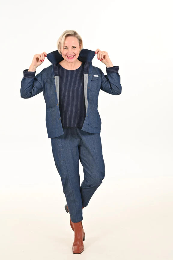 Front view of a woman wearing the Alice Cocoon Pants by Julei Design in Denim with a blue jacket, standing in front of a white background 