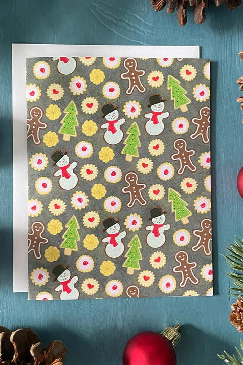 A Christmas Cookies card from a box set by Carabara Designs, featuring a cute cookie design, is shown against a teal background with holiday decor surrounding it.  