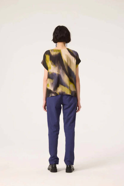 Back view of a woman wearing the Fuzzy Top by Cokluch in Vertigo print with blue pants, standing in front of a white background 