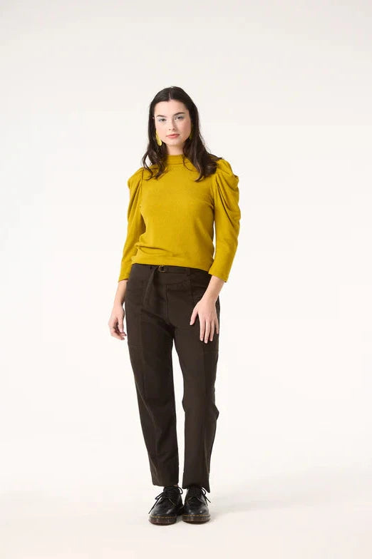 A woman wearing the Nenuphar Top by Cokluch in Avocado, featuring a high collar and 3/4 length puffed sleeves, with the Belief Pants in Pine. She's standing in front of a white background. 